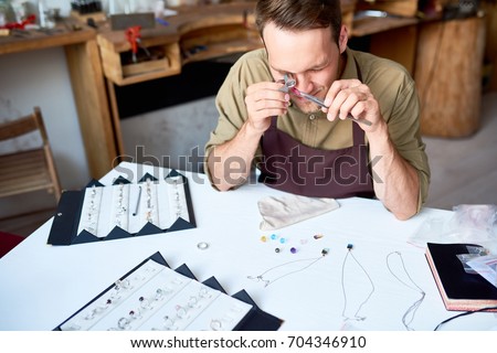Portrait of young man inspecting jeweler with magnifying glass while appraising goods in pawn shop