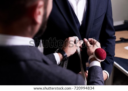 Over shoulder view of bearded fashion designer fitting bespoke suit to model, close-up shot