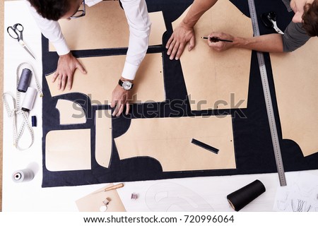 High angle view of concentrated young tailors using sewing patterns while working on creation of custom-made male jacket