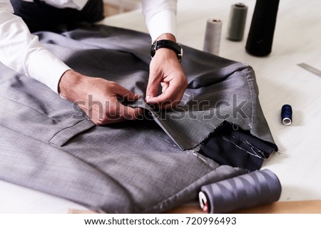 Production process of custom-made male jacket: unrecognizable tailor concentrated on sewing with needle and thread, close-up shot
