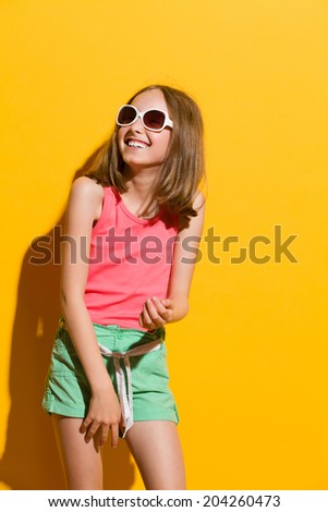 Laughing young summer girl looking away. Three quarter length studio shot on yellow background.