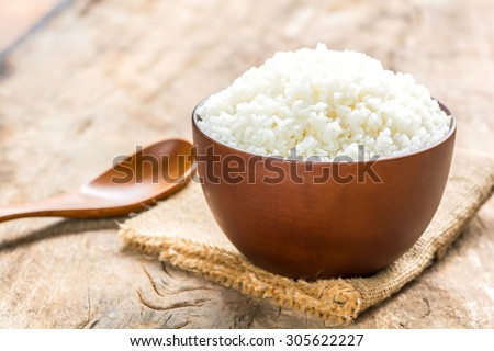 Cooked rice in bowl with spoon on old wooden table