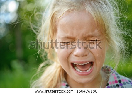 Beautiful sad little girl crying, on summer background.