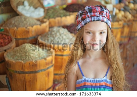 Portrait of beautiful smiling little girl against background of wooden barrels and spices.
