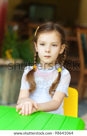 Little girl sits at green children's table and thinking.