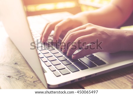 Side view shot of beautiful young hipster woman's hands busy working on her laptop sitting at wooden table in a coffee shop - retro filter effect and vintage color style