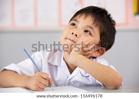 Male Student Working At Desk In Chinese School Classroom