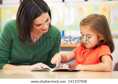 Elementary Pupil Reading With Teacher In Classroom
