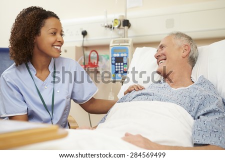 Nurse Sitting By Male Patient's Bed In Hospital