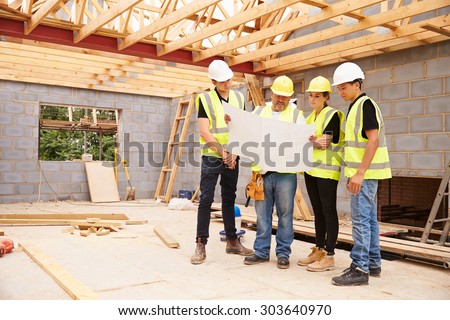 Builder On Building Site Looking At Plans With Apprentices