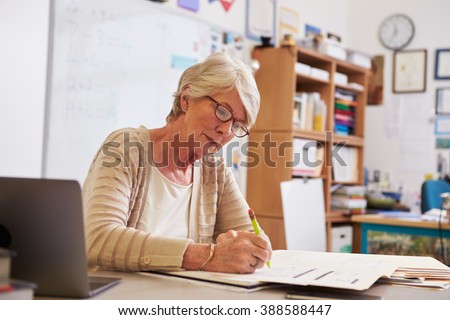 Senior female teacher at her desk marking studentsâ?? work