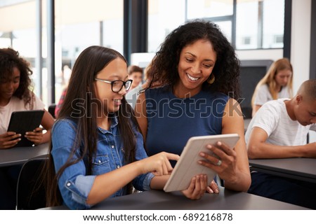 Teacher helping teenage schoolgirl with tablet computer