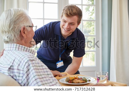 Male care worker serving dinner to a senior man at his home
