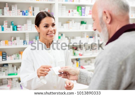 Beautiful young pharmacist selling medications to senior patient