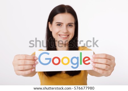 Kiev, Ukraine - August 22, 2016: Woman hands holding colorful Google logotype printed on paper on grey background. Google is USA multinational corporation.