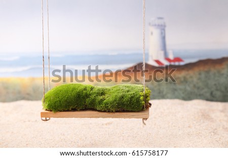 A newborn baby photography backdrop prop of a moss covered swing and the beach with a lighthouse and ocean waves in the background.