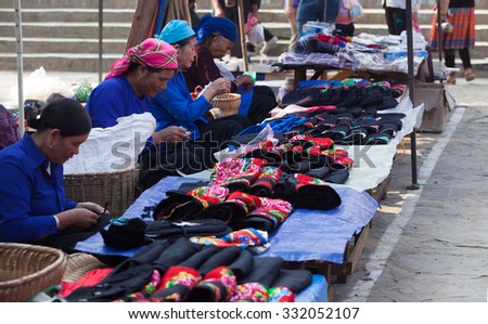 Lao Cai, Vietnam - Oct 17, 2015: Asian senior tailors sewing and selling colorful traditional textile products at Bac Ha weekly flea market, north west of Vietnam.