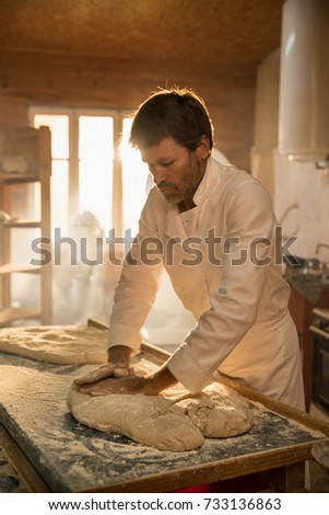 in an artisan bakery, the baker kneads the dough for the bread. The morning sun comes in through the window