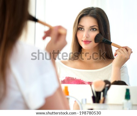 Beauty woman applying makeup. Beautiful girl looking in the mirror and applying cosmetic with a big brush. Girl gets blush on the cheekbones. Powder, rouge