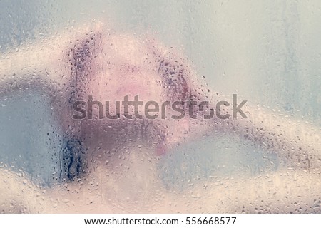 Beautiful woman in the shower behind glass with drops