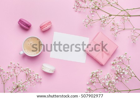 Morning cup of coffee, cake macaron, gift or present box and flower on pink table from above. Beautiful breakfast. Flat lay style.