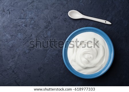 Greek yogurt in blue bowl on black table top view.