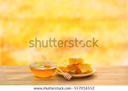 Honey in glass bowl, wooden honey dipper and honeycombs with honey on wooden table on background honeycombs with full cells of honey