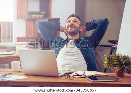 Satisfied with work done. Happy young man working on laptop while sitting at his working place in office