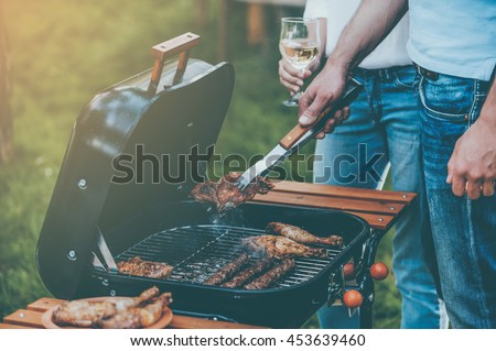 Barbecuing to perfection. Close-up of two people barbecuing meat on the grill while standing outdoors