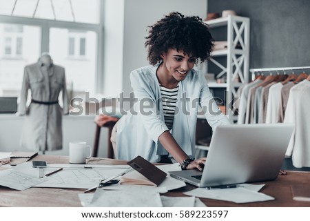 Responding on business e-mail. Beautiful young African woman working using computer and smiling while standing in workshop