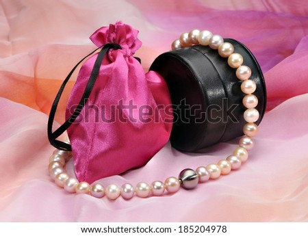 Pearl necklace, black leather case and a pink bag on a colored background.
