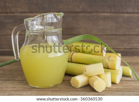 Fresh squeezed sugar cane juice in pitcher with cut pieces cane on wooden background.