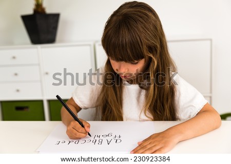 Young caucasian girl with long hair writing letters on a white piece of paper.