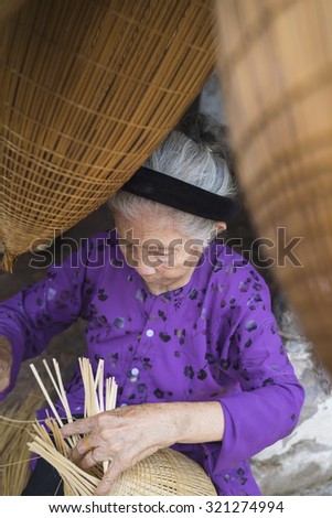 Hung Yen, Vietnam - July 26, 2015: Old woman weaves bamboo fish trap at Vietnamese traditional crafts village Thu Sy, Hung Yen province.