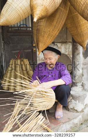 Hung Yen, Vietnam - July 26, 2015: Old woman weaves bamboo fish trap at Vietnamese traditional crafts village Thu Sy, Hung Yen province.