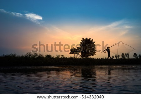 Hung Yen, Vietnam - July 9, 2016: Vietnamese rural countryside sunset scene with silhouette farmers carrying bamboo fish traps home in Thu Sy village