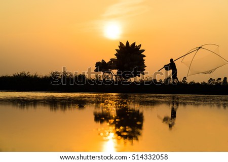 Hung Yen, Vietnam - July 9, 2016: Vietnamese rural countryside sunset scene with silhouette farmers carrying bamboo fish traps home in Thu Sy village