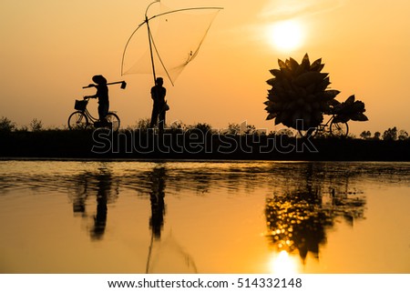 Hung Yen, Vietnam - July 9, 2016: Vietnamese rural countryside sunset scene with silhouette farmers carrying bamboo fish traps home in Thu Sy village
