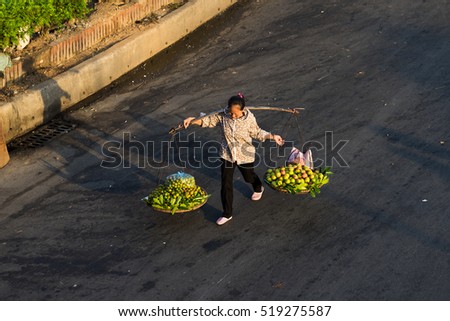 Hanoi, Vietnam - July 23, 2016: Aerial view of Vietnamese woman vendor carrying fruit on balance on Yen Phu street in early morning