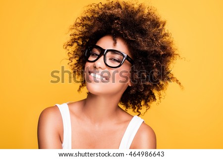 Young beautiful african american girl with an afro hairstyle. Laughing girl wearing eyeglasses. Portrait. Yellow background. Girl looking at camera.