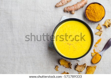 Turmeric drink, latte, tea, milk with cinnamon in a glass mug with fresh and dried turmeric on a textile grey background. Top view. Copy space.