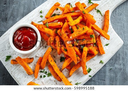 Healthy Homemade Baked Orange Sweet Potato Fries with ketchup, salt, pepper on white wooden board