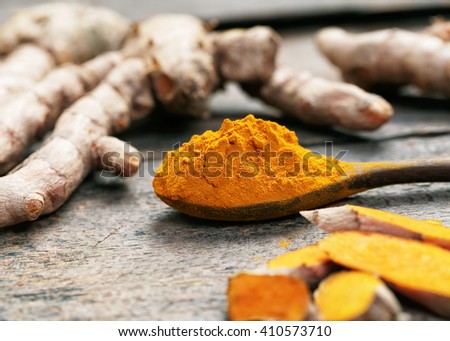 Turmeric powder and turmeric on wooden spoon.