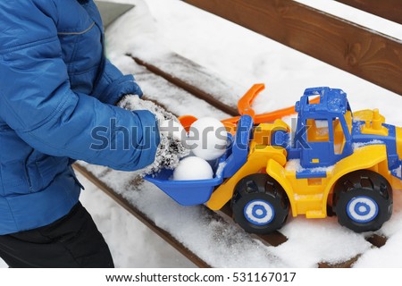Children's winter games outdoors. The image of a child making snow snow balls and playing with a large colourful toy car.