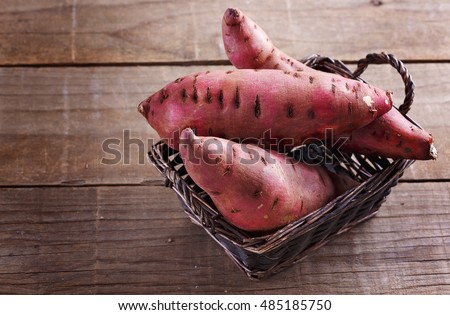 Red Sweet potato in a woven basket over rustic wooden background closeup