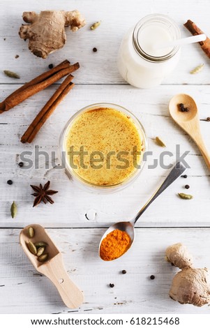 Top view image of turmeric latte, spices and bottle of milk over white wooden table