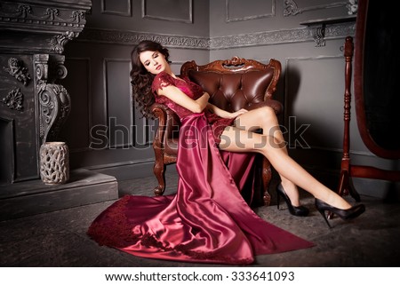 Woman sitting in chair in long claret dress. Luxury