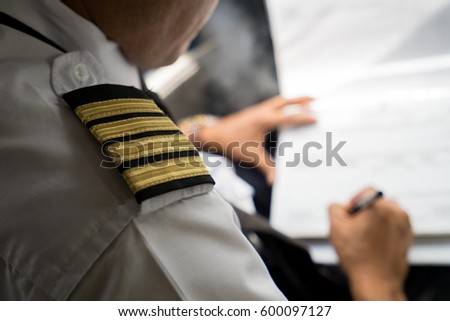 Captain in the aircraft cockpit writing a report after flight. Focusing on his pilot epaulets.