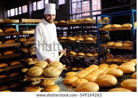 young handsome guy baker pulls out of the oven fresh bread at the bakery background