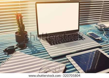 Freelance desktop with accessories and distance work tools, blank screen laptop computer and digital tablet, mouse, sunglasses, phone charging and touch pad, business workspace in home or office